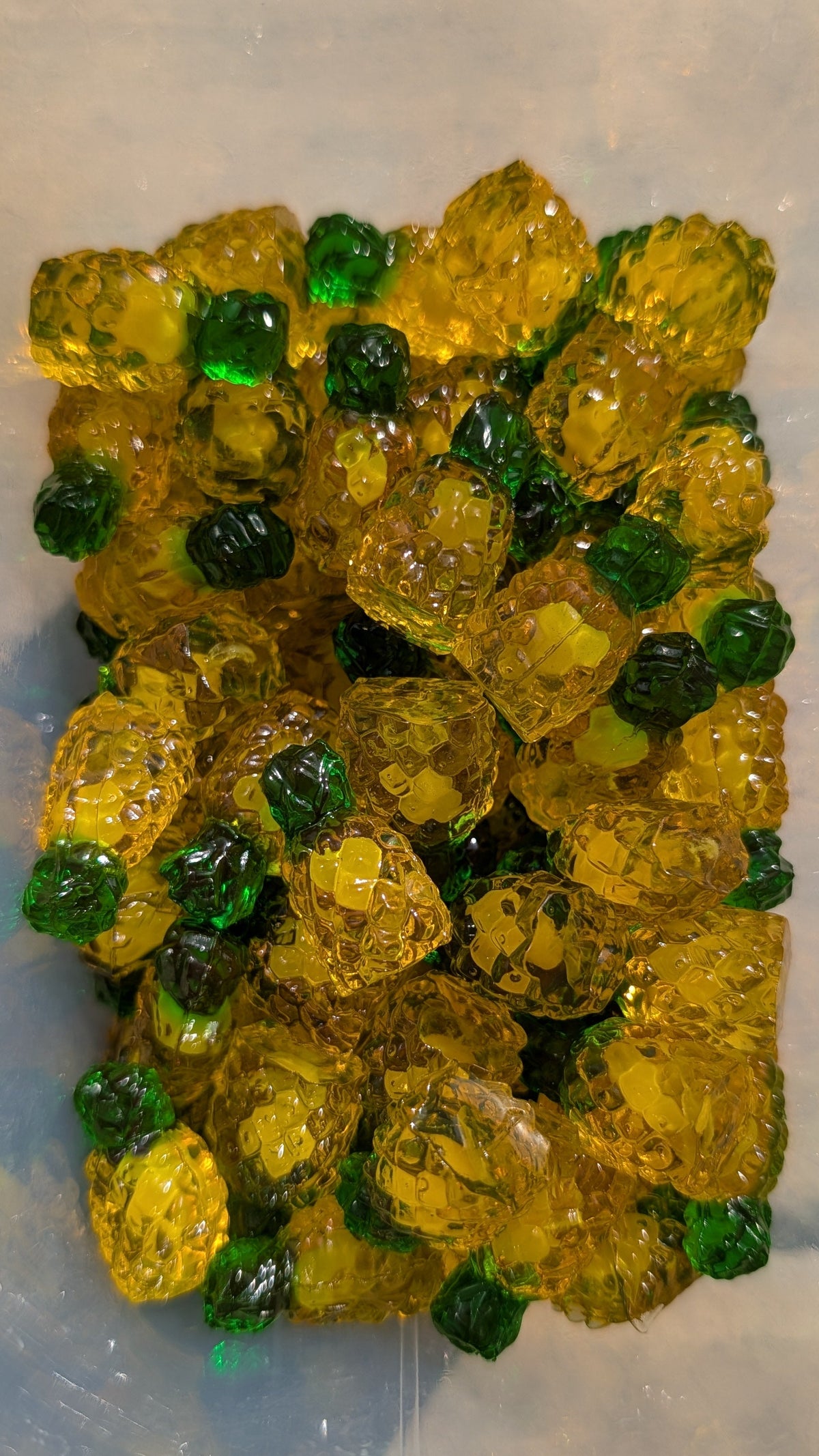 A pile of translucent yellow gel beads with small dark green accents, photographed on a light gray surface.
